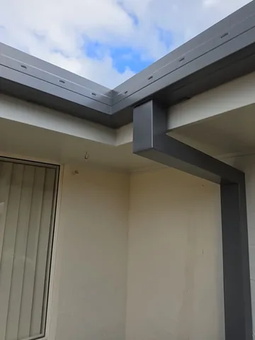 New grey guttering and downpipe on a white rendered eave corner